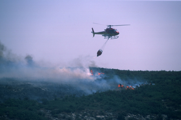 An Airbus-produced H125 helicopter deploys a bucket-type water dispersal system to support firefighting efforts. An Airbus-produced H125 helicopter deploys a bucket-type water dispersal system to support firefighting efforts.