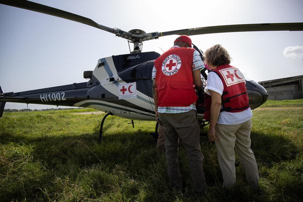 Airbus Foundation annual activity report 2023 cover image Two people standing in front of a helicopter with their back to the camera, both wear Red Cross / Red Crescent societies gear