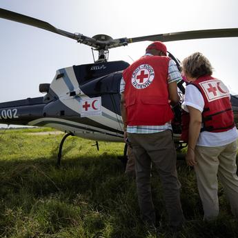 Two people standing in front of a helicopter with their back to the camera, both wear Red Cross / Red Crescent societies gear