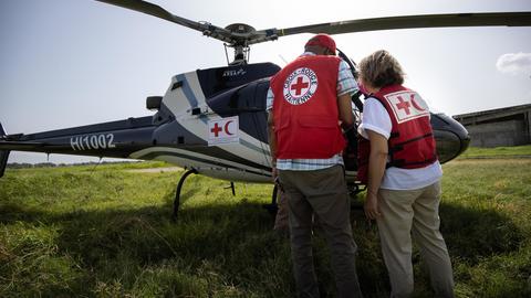 Two people standing in front of a helicopter with their back to the camera, both wear Red Cross / Red Crescent societies gear