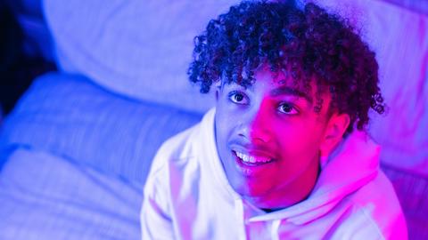 Young man looks up with a curious look, lit by a pink light