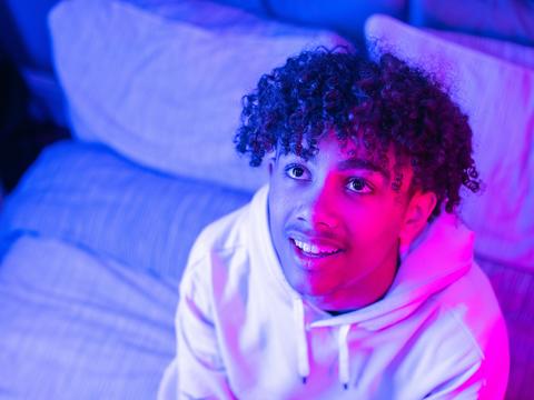 Young man looks up with a curious look, lit by a pink light