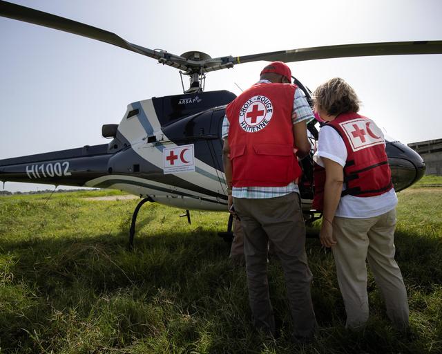 Airbus Foundation annual activity report 2023 cover image Two people standing in front of a helicopter with their back to the camera, both wear Red Cross / Red Crescent societies gear