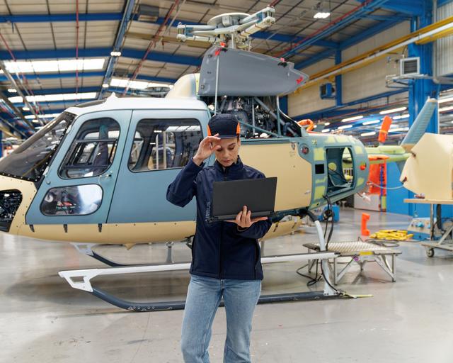 Woman wearing PPE stands in front of a helicopter looking at a laptop
