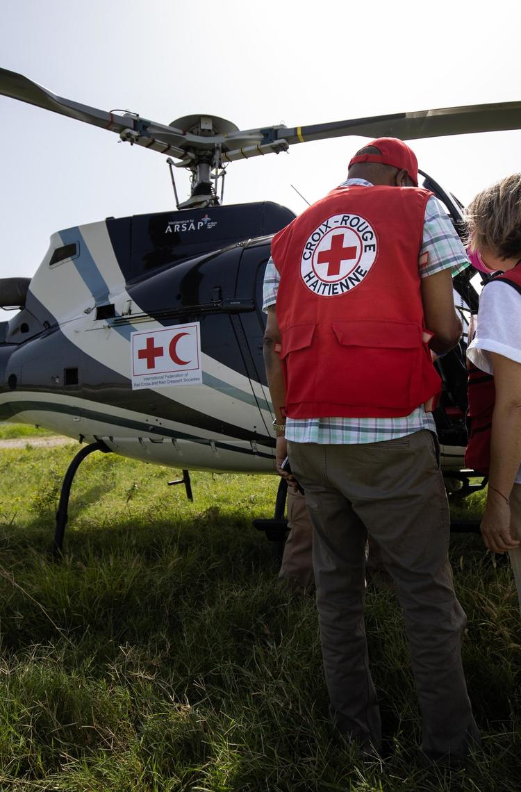 Two people standing in front of a helicopter with their back to the camera, both wear Red Cross / Red Crescent societies gear