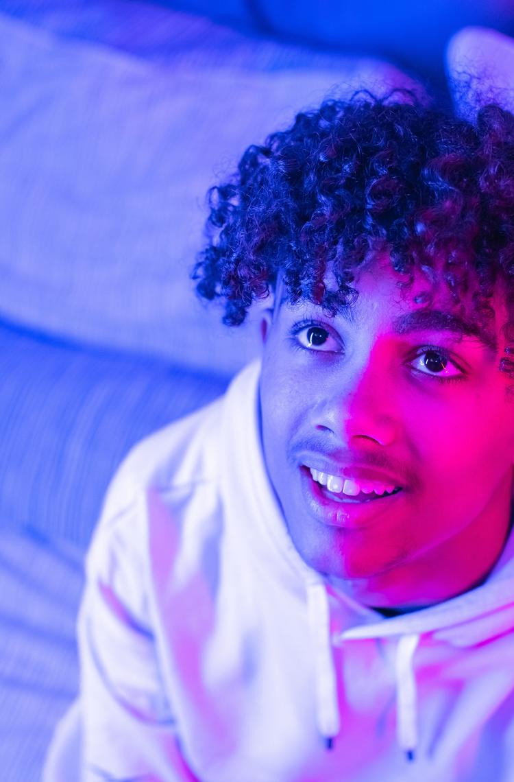 Young man looks up with a curious look, lit by a pink light