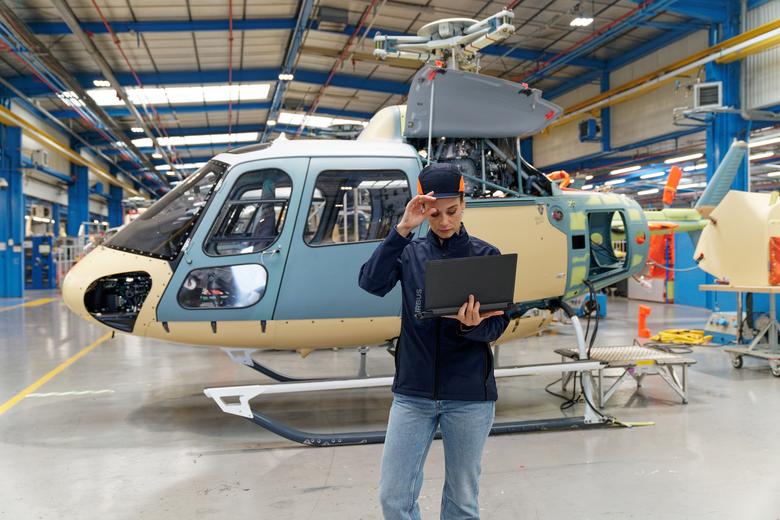 Woman wearing PPE stands in front of a helicopter looking at a laptop