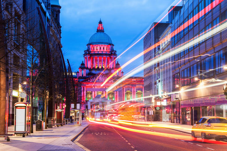 Cityscape at night focused on Belfast City Hall, with long exposure camera showing the light streams of passing cars and buses